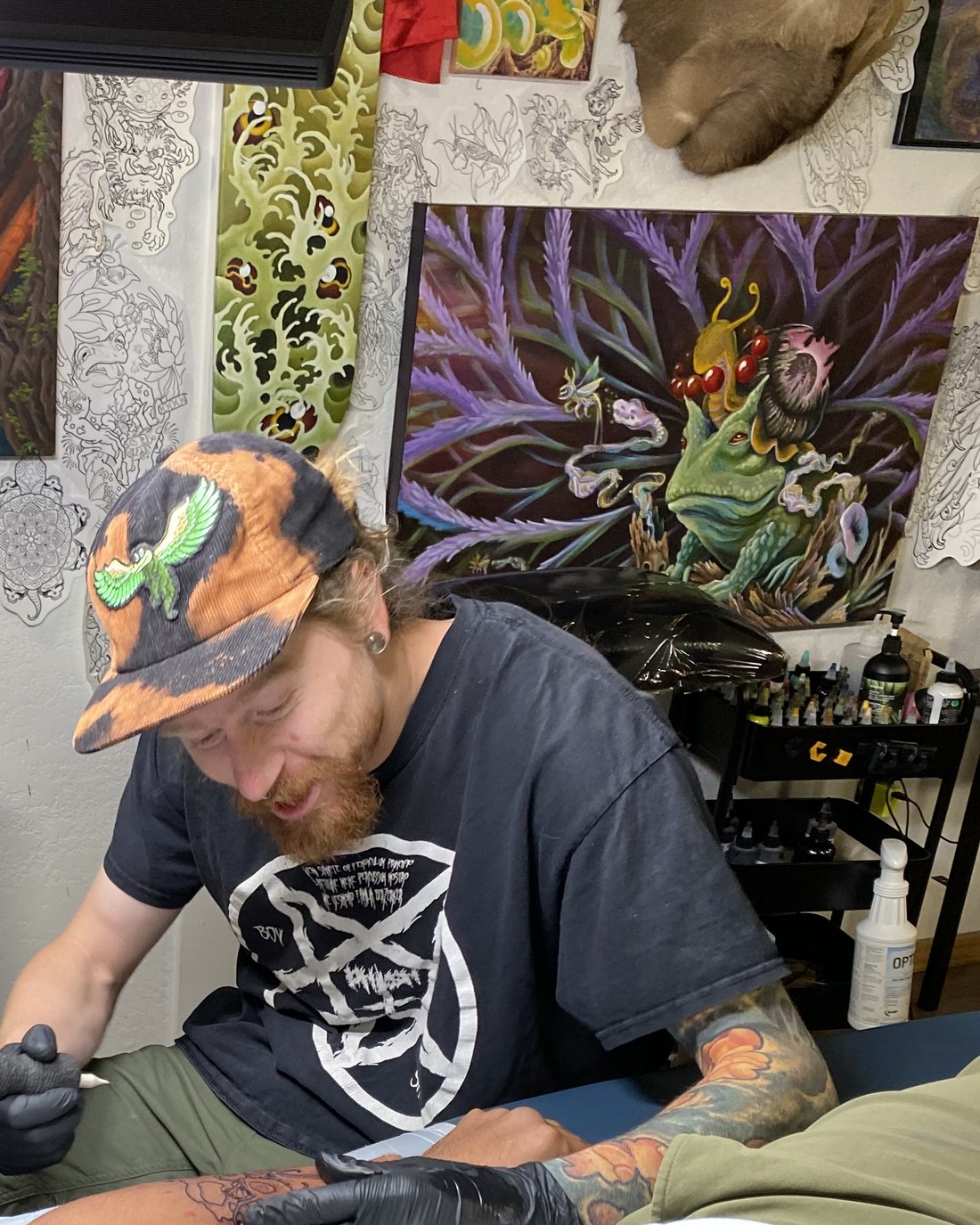 Jamie Thompson tattooing in front of his bio-organic paintings in the studio