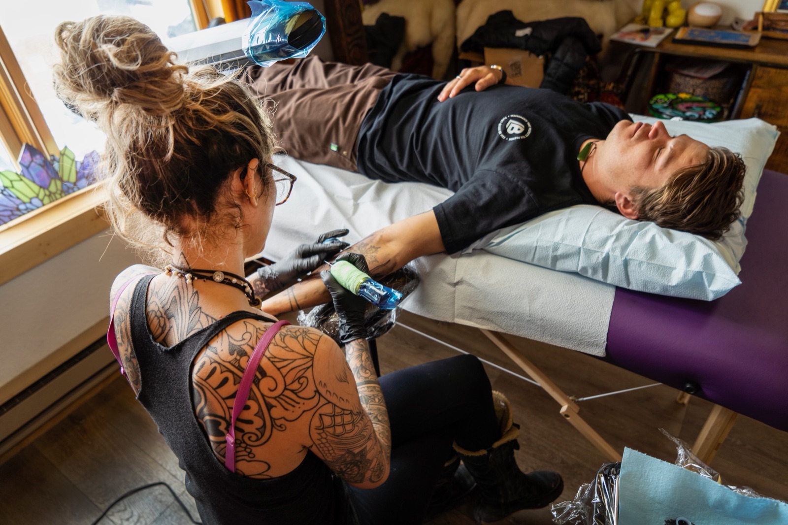 Janice tattooing a client’s arm in a sunlit studio