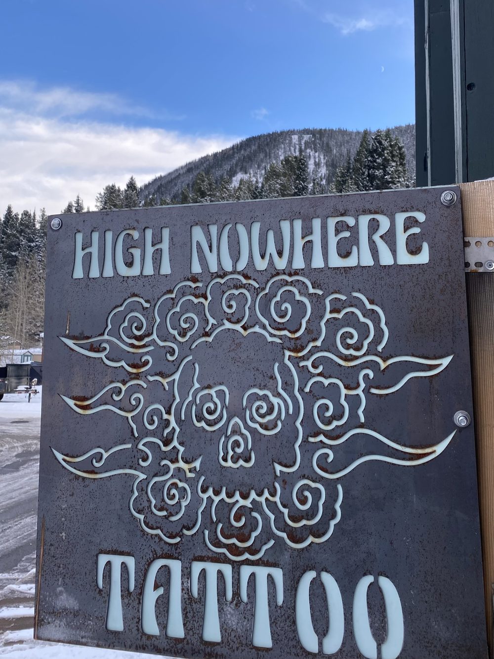 The rusted steel High Nowhere Tattoo sign against a snowy mountain
