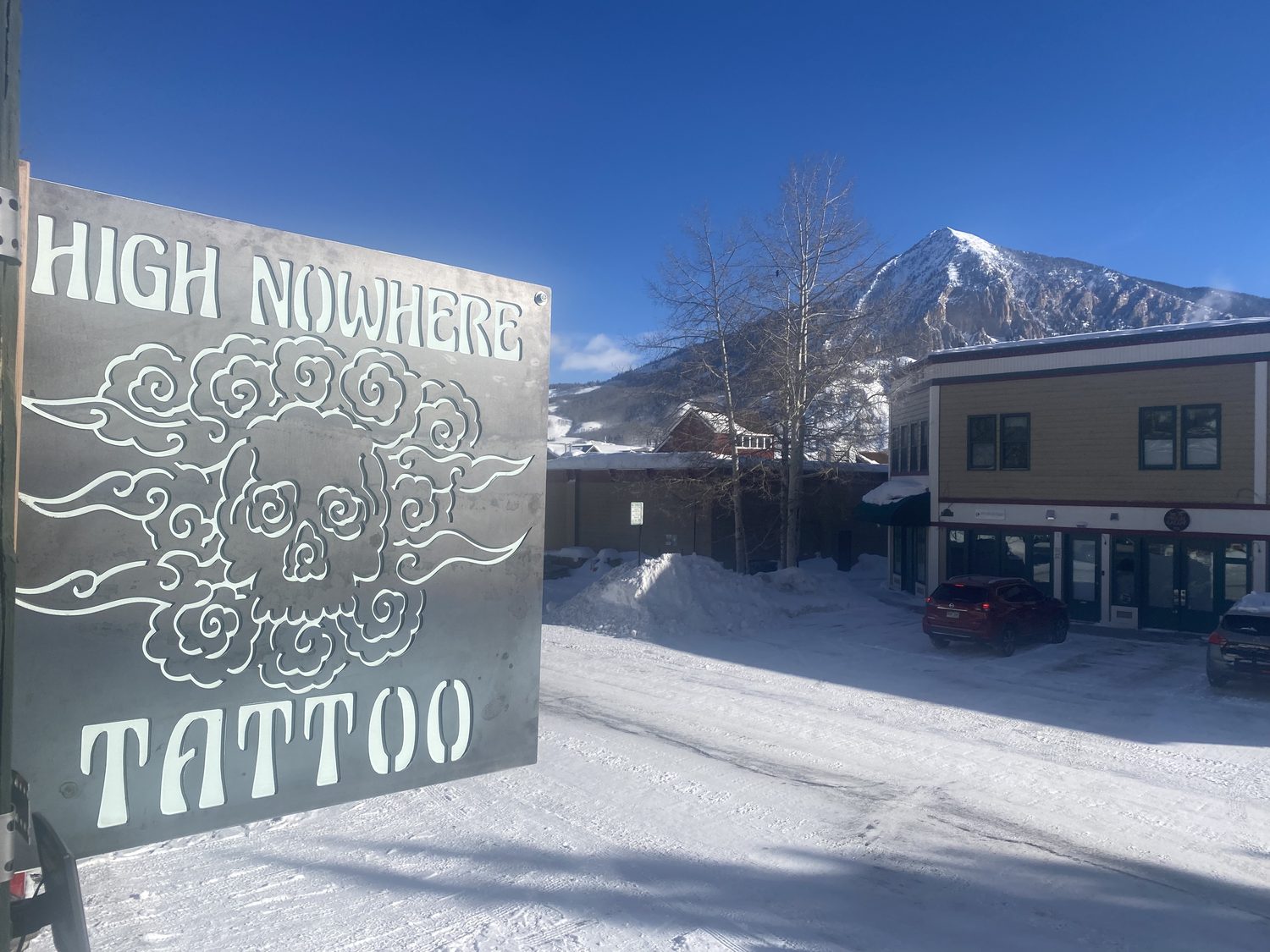 The High Nowhere Tattoo steel sign outside the studio with Mt. Crested Butte behind