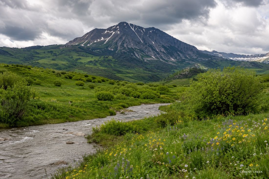 A creek winding through green hills below the peaks at Cement Creek