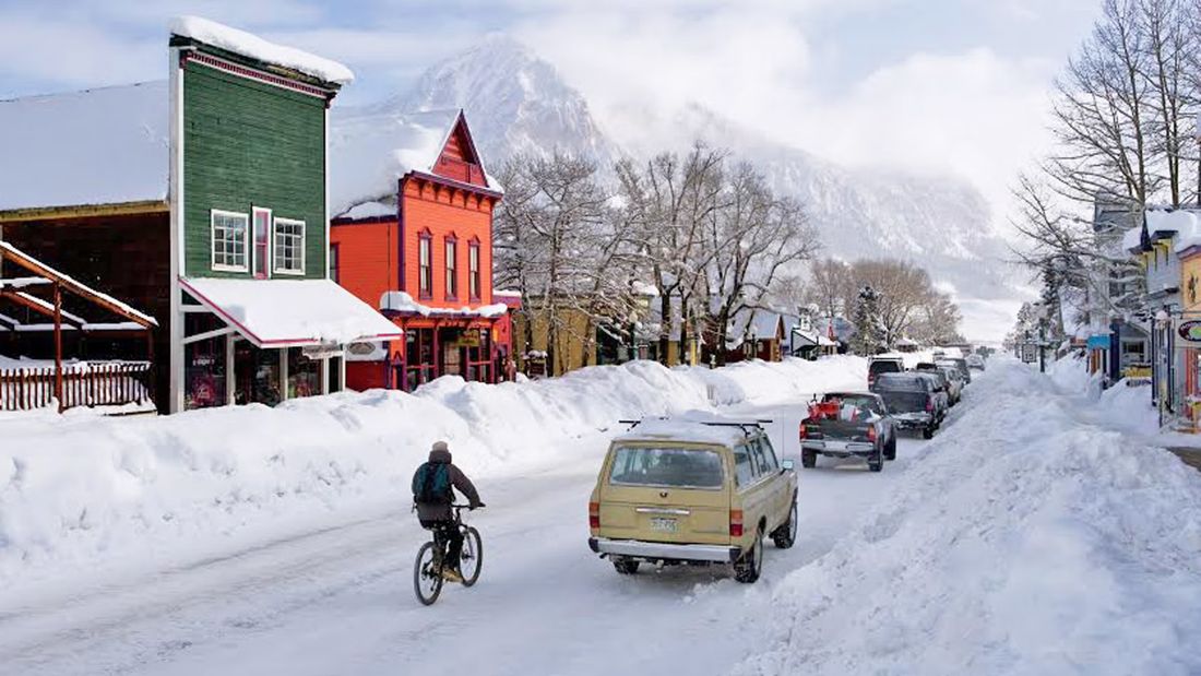 A cyclist on snowy Elk Avenue past colorful historic buildings in winter