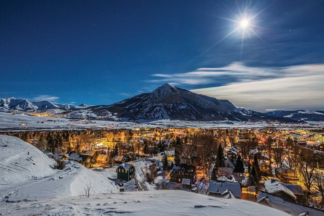 Full moon over the lights of Crested Butte at night with Mt. Crested Butte beyond