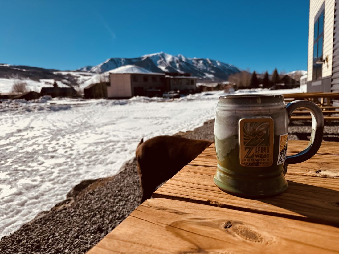 A coffee mug on a deck rail with a snowy mountain view in town